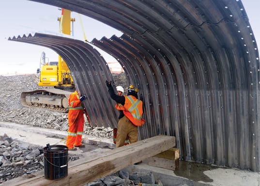 buried metal bridge corrugated panel being installed by three workers